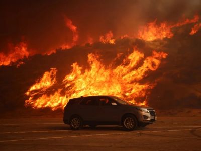 Автомобиль проезжает мимо холма, охваченного пламенем. Фото: Ethan Swope / AP